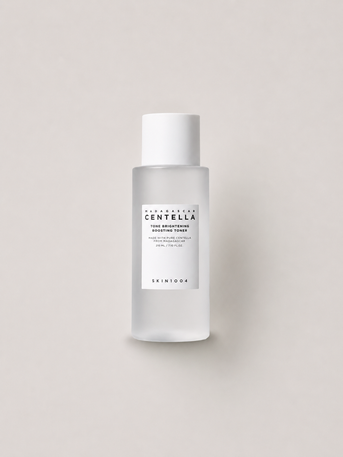 A bottle of Korean skincare toner - SKIN1004 Madagascar Centella Tone brightening Boosting Toner, featuring a frosted glass bottle and a white cap, set against a solid light beige background. 210 ml.