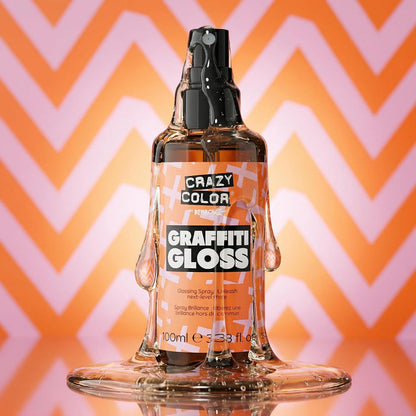 a texture visual of Crazy Color Graffiti Gloss Glossing Spray 100ml with the liquid leaking out the spray lid going down onto the product and a puddle of liquid at the bottom on a pink and orange triangular patterned background