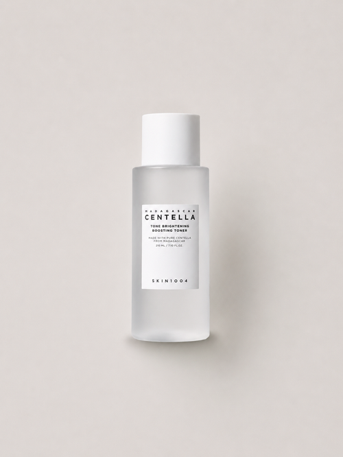 A bottle of Korean skincare toner -  SKIN1004 Madagascar Centella Tone brightening Boosting Toner, featuring a frosted glass bottle and a white cap, set against a solid light beige background. 210 ml.